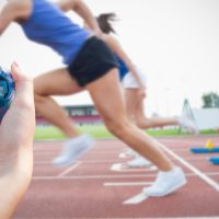 Sprinters leaving the starting blocks as a hand holds a stopwatch
