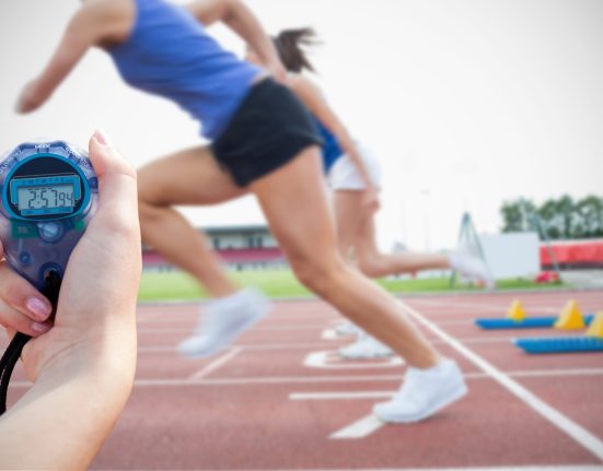 Sprinters leaving the starting blocks as a hand holds a stopwatch