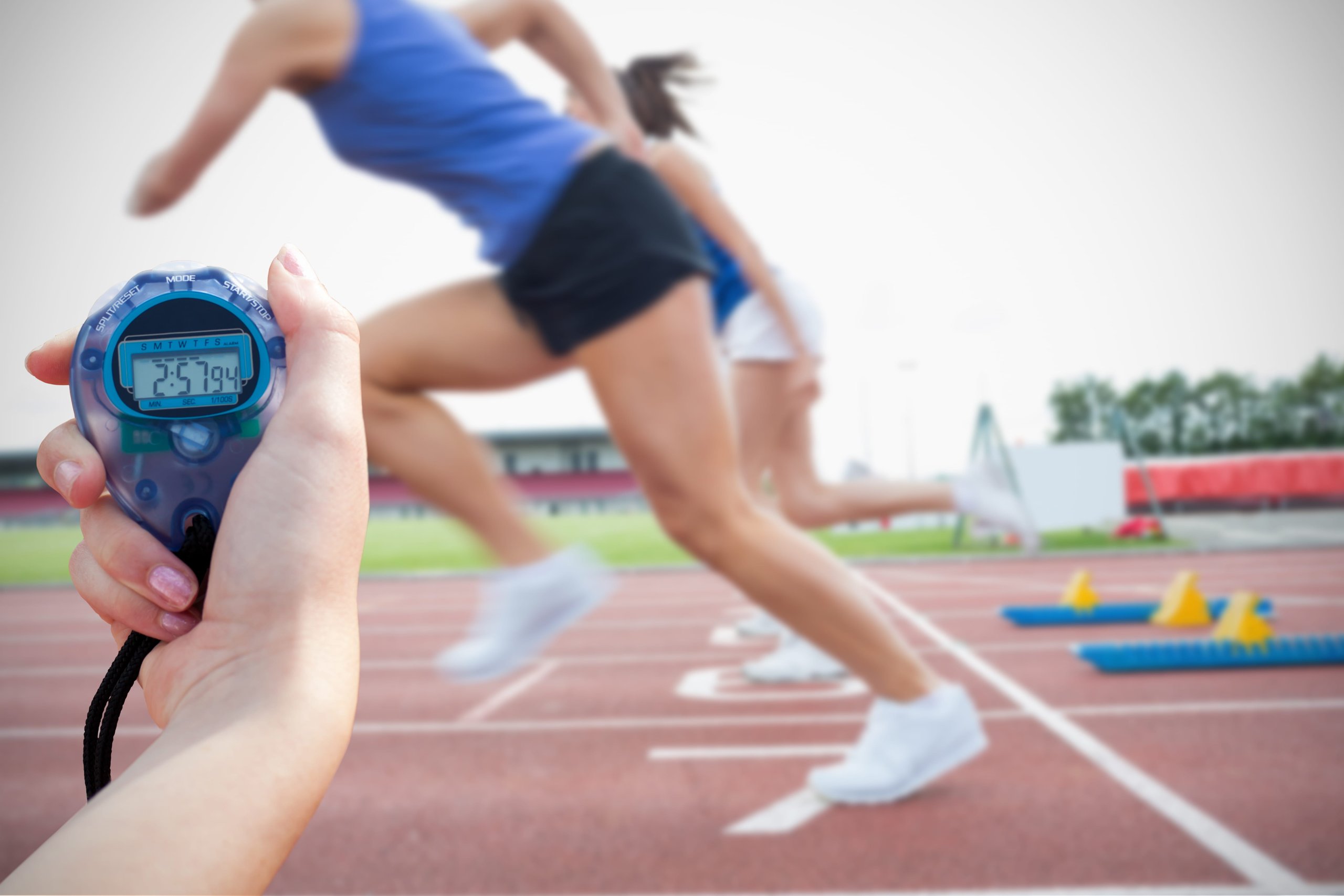 Sprinters leaving the starting blocks as a hand holds a stopwatch