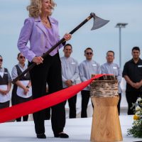 A woman holding a ceremonial axe beside a red ribbon at a ship ceremony