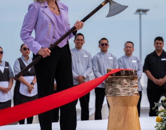 A woman holding a ceremonial axe beside a red ribbon at a ship ceremony