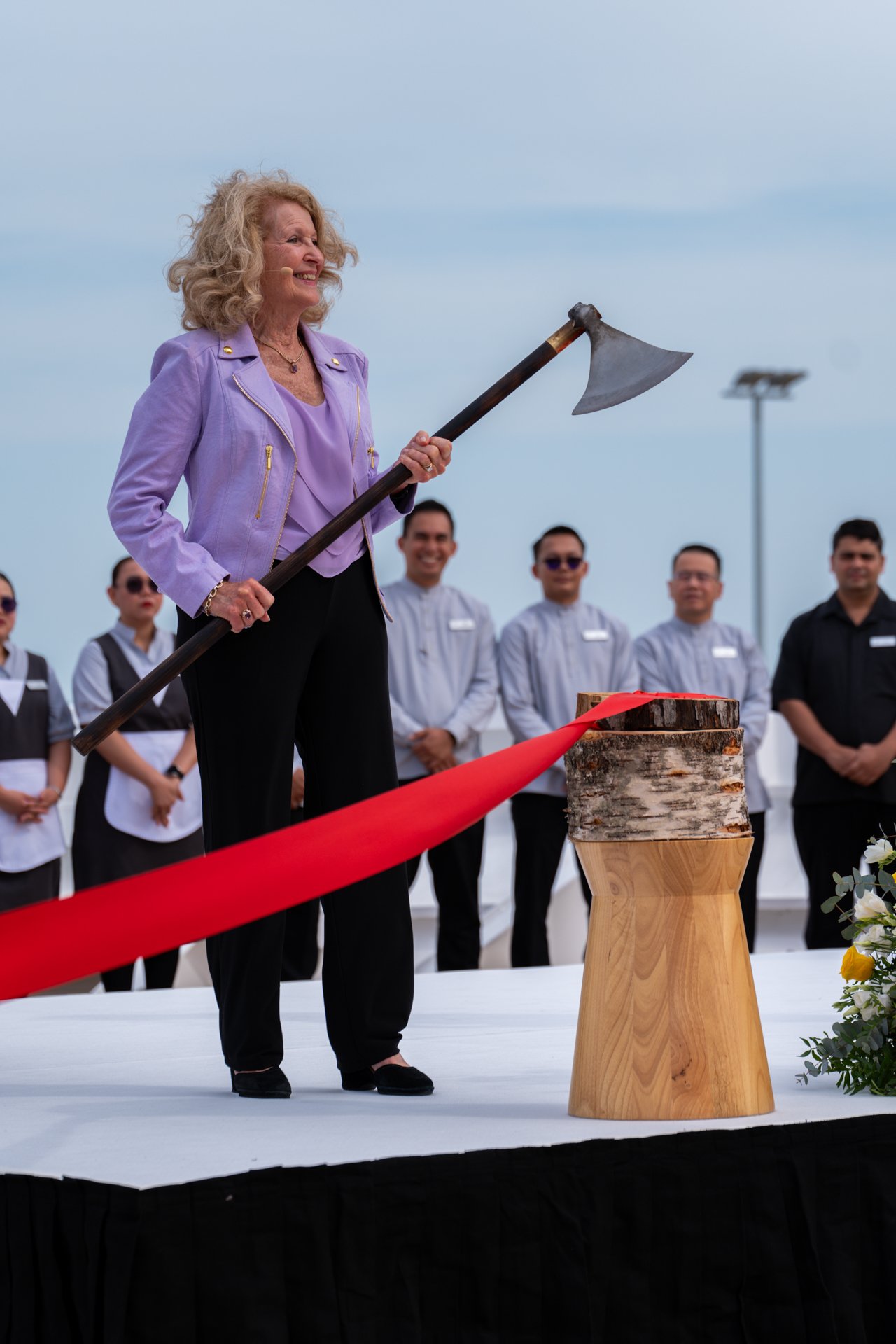 A woman holding a ceremonial axe beside a red ribbon at a ship ceremony